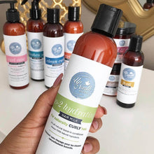 Load image into Gallery viewer, Woman holding go-2 hydrating hair milk in front of a gold trim mirror and other up north natural products in the background